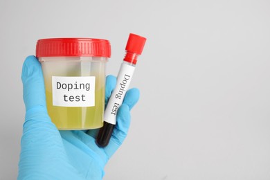 Photo of Closeup view of doctor holding jar and test tube with samples on light grey background, space for text. Doping control