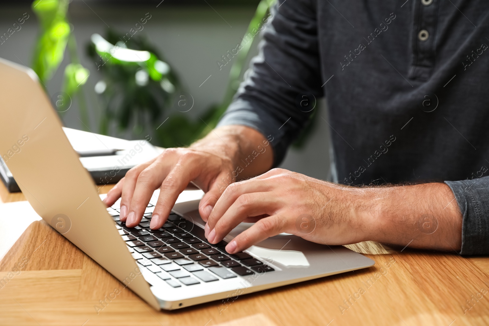 Photo of Man using laptop for search at wooden table indoors, closeup
