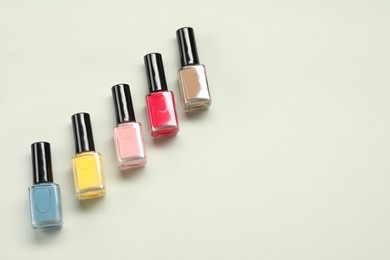 Colorful nail polishes in bottles on light background, flat lay. Space for text