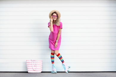 Happy young woman with retro roller skates near white garage door