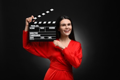 Photo of Happy actress with clapperboard on black background. Film industry