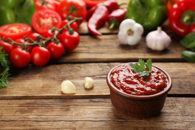 Photo of Delicious adjika sauce in bowl and ingredients on wooden table