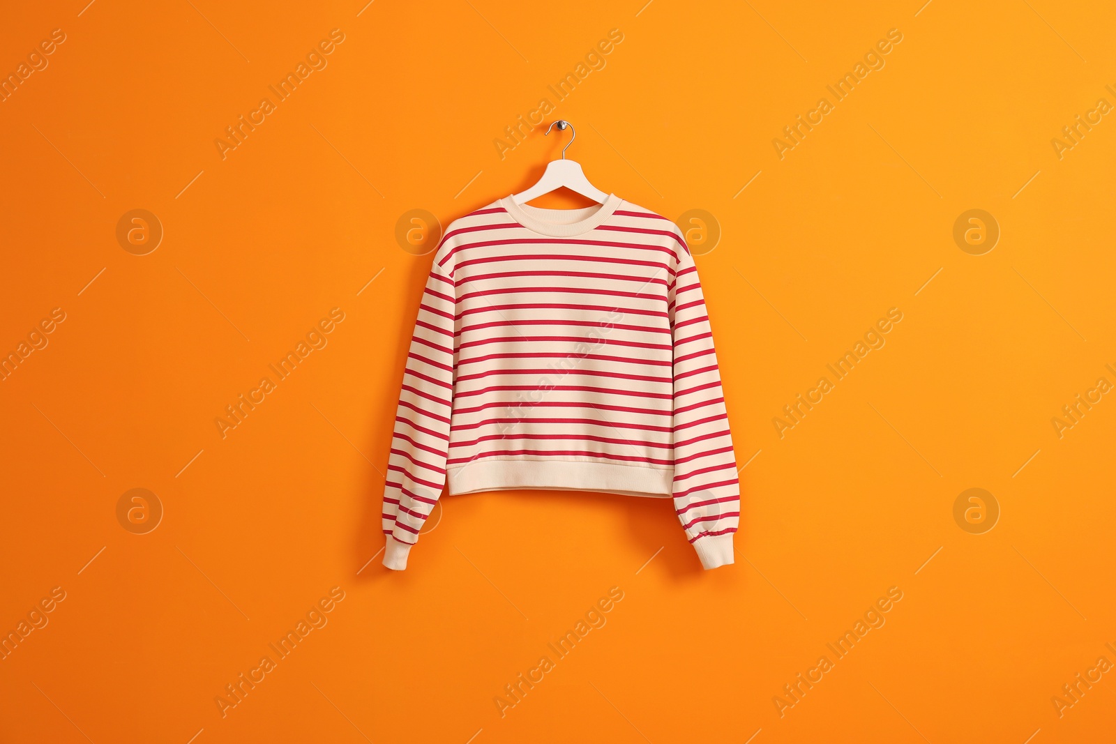 Photo of Hanger with striped sweatshirt on orange wall