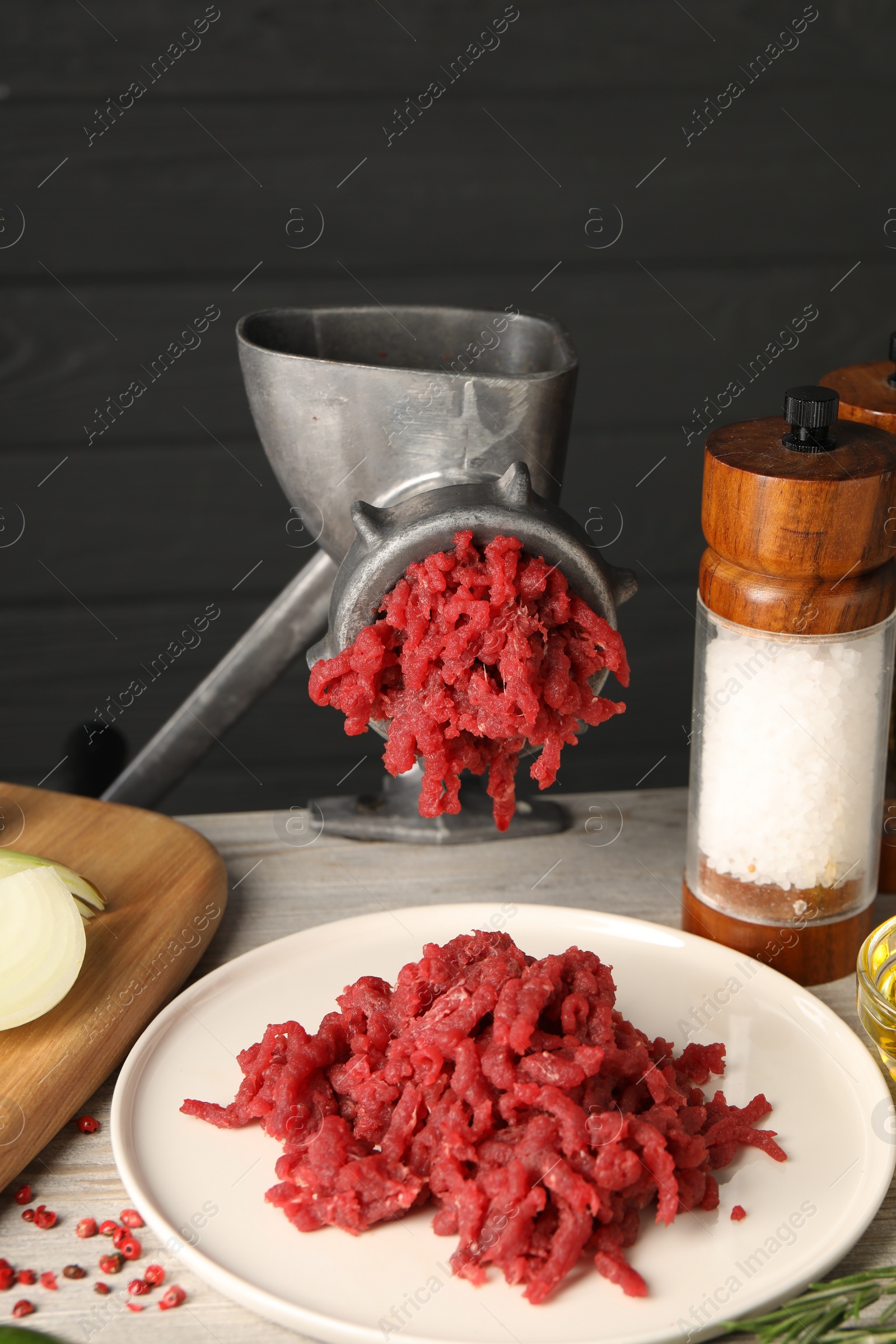 Photo of Metal meat grinder with minced beef and salt on light wooden table