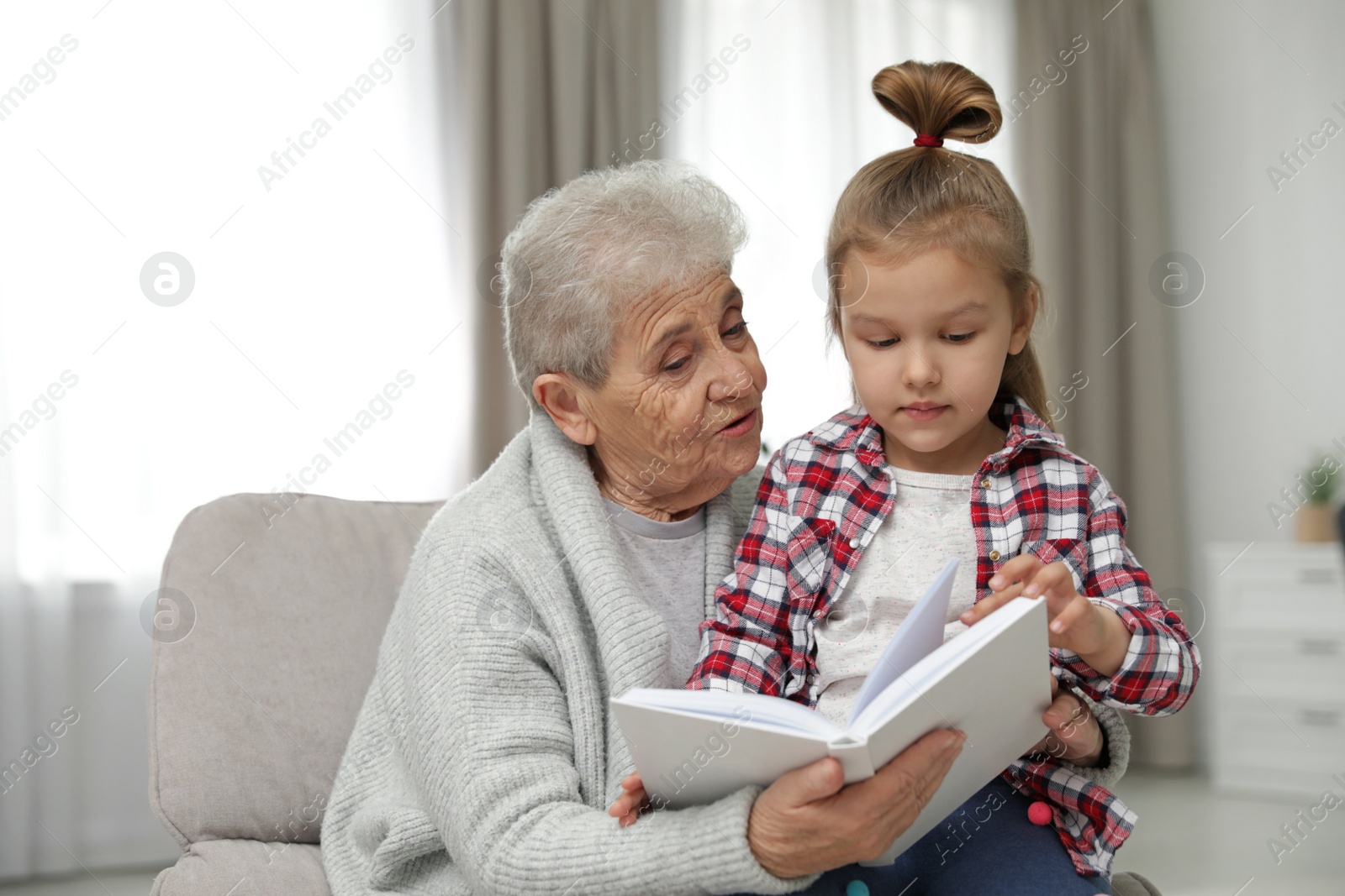 Photo of Cute girl and her grandmother reading book at home