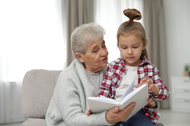 Photo of Cute girl and her grandmother reading book at home