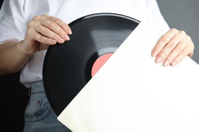 Photo of Woman taking vinyl record out of paper sleeve on grey background, closeup