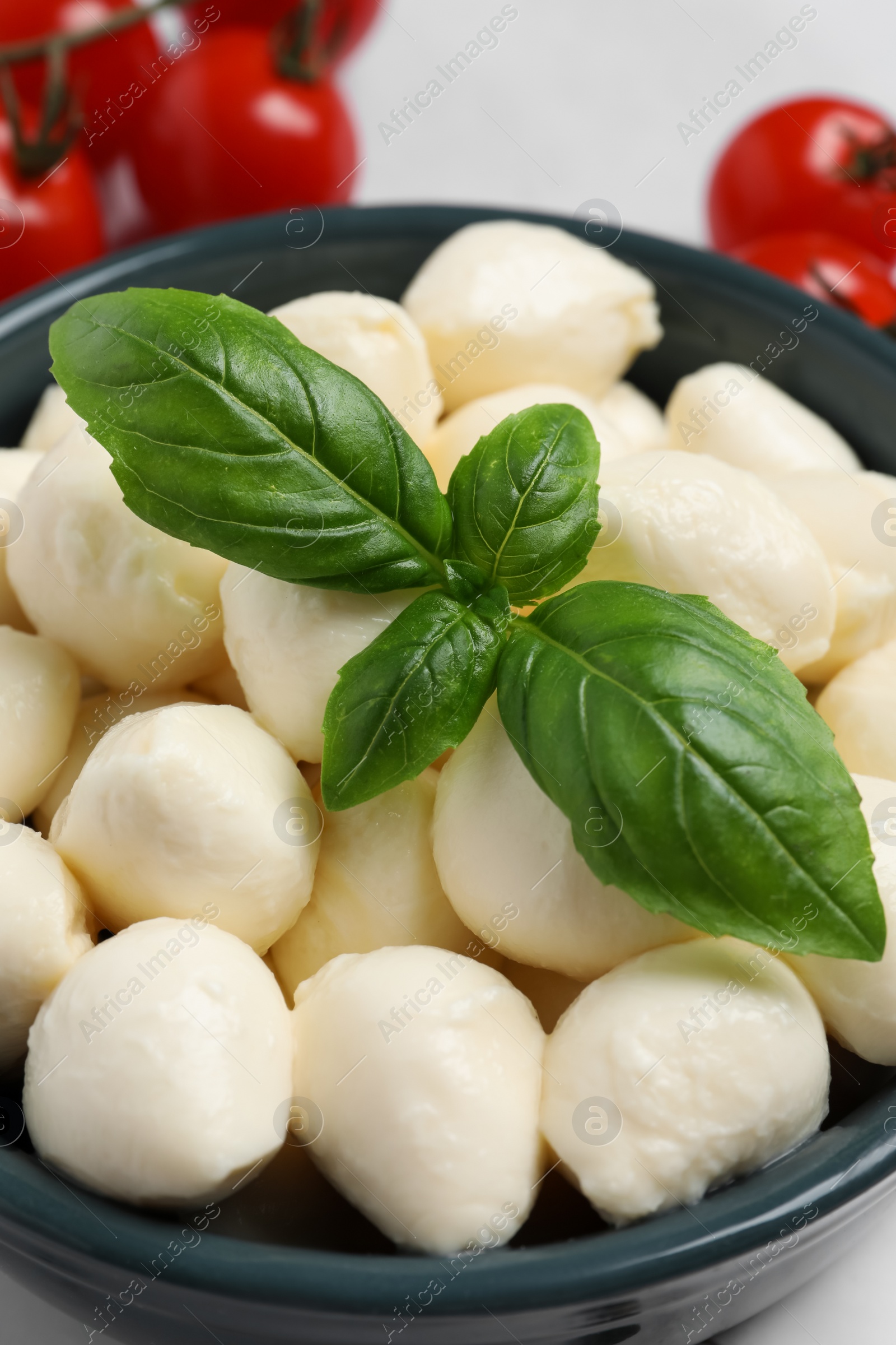 Photo of Delicious mozzarella balls and basil leaves in bowl, closeup