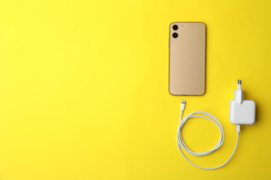 Photo of Smartphone and USB charger on yellow background, flat lay. Space for text