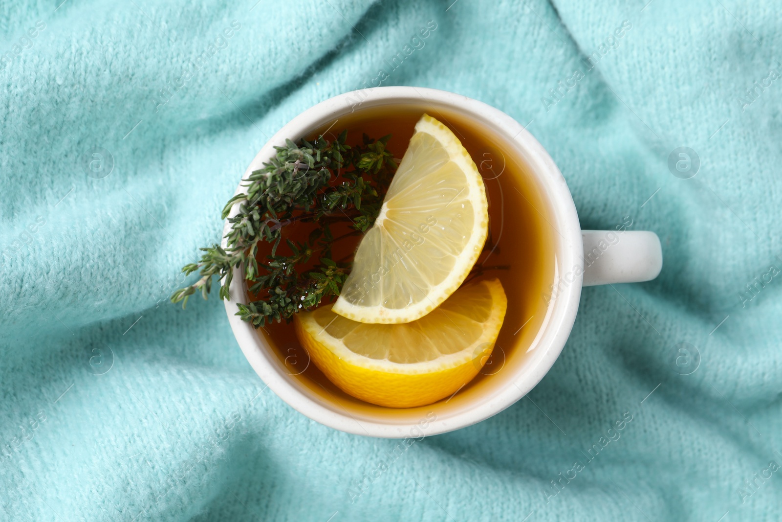 Photo of Cup of tasty herbal tea with thyme and lemon on turquoise fabric, top view