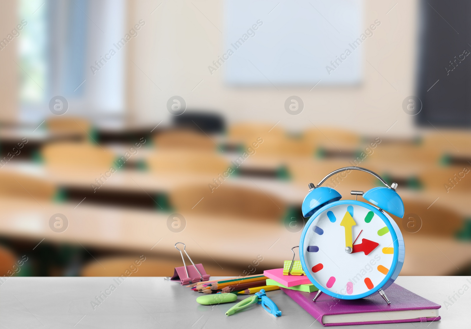 Image of Light blue alarm clock and different stationery on white table in classroom, space for text