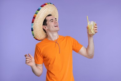 Photo of Young man in Mexican sombrero hat with cocktail on violet background