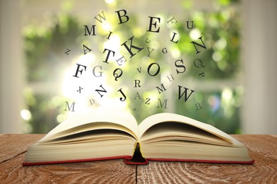 Image of Open book with letters flying out of it on wooden table against blurred background