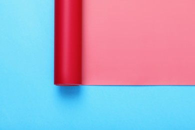 Photo of Roll of red wrapping paper on light blue background, top view. Space for text