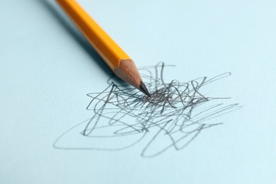 Photo of One sharp graphite pencil and scribbles on light blue background, closeup