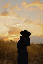 Mother with baby walking outdoors at sunset, silhouette