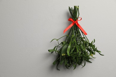 Photo of Mistletoe bunch with red bow on light grey table, top view and space for text. Traditional Christmas decor