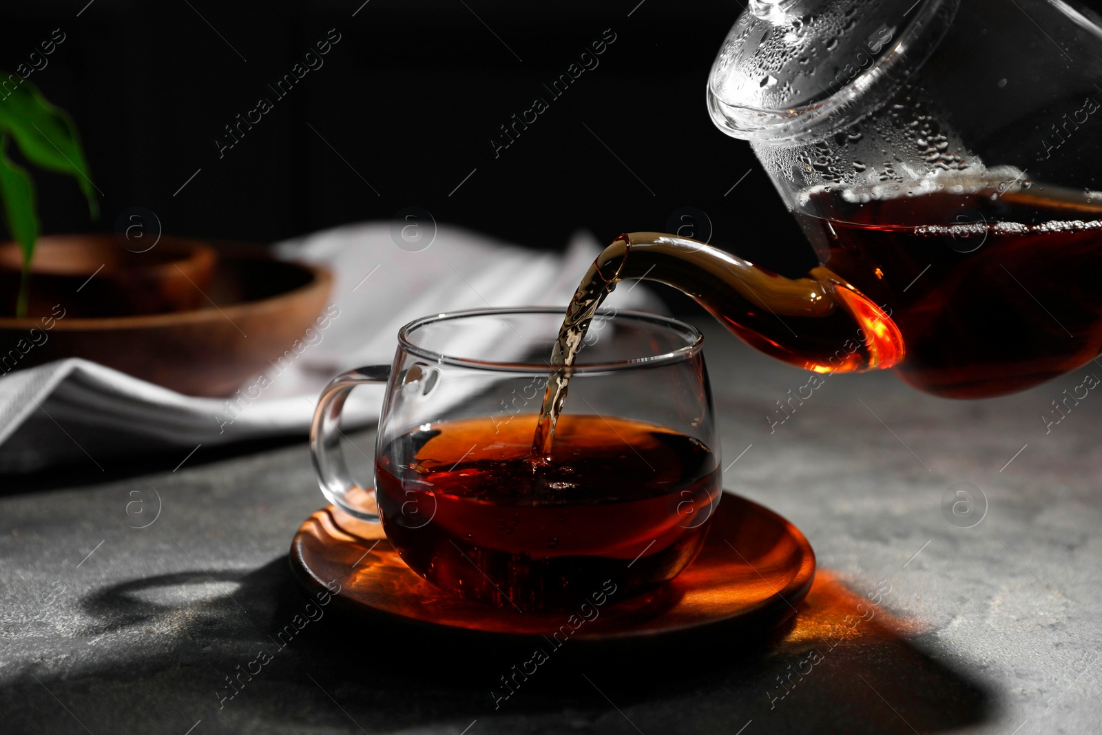 Photo of Pouring hot tea into cup on grey table, closeup