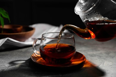 Photo of Pouring hot tea into cup on grey table, closeup