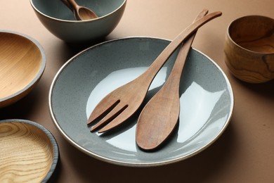 Stylish empty dishware and wooden cutlery on brown background