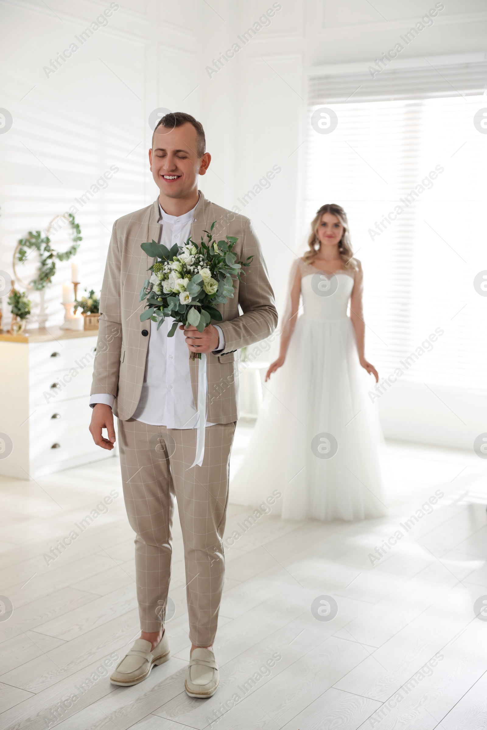 Photo of Groom with closed eyes waiting for his lovely bride indoors. First meeting at wedding day