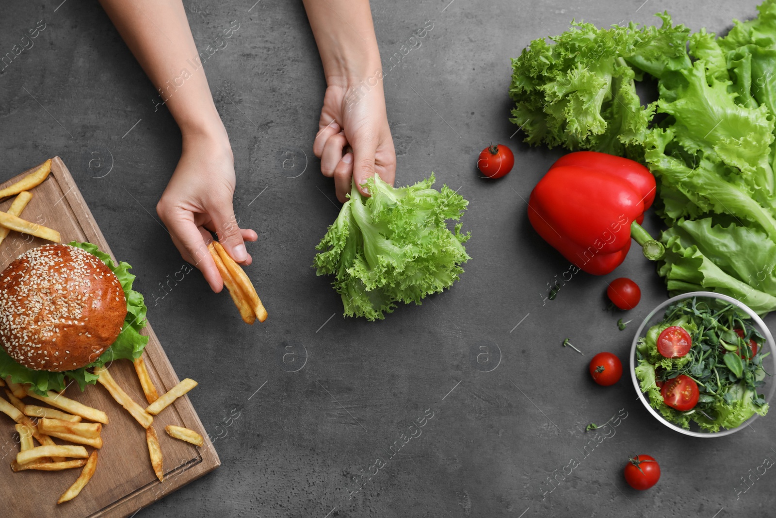 Photo of Top view of woman choosing between vegetables and French fries with burger at black table, closeup