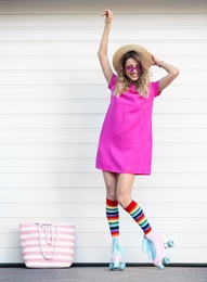 Happy young woman with retro roller skates near white garage door