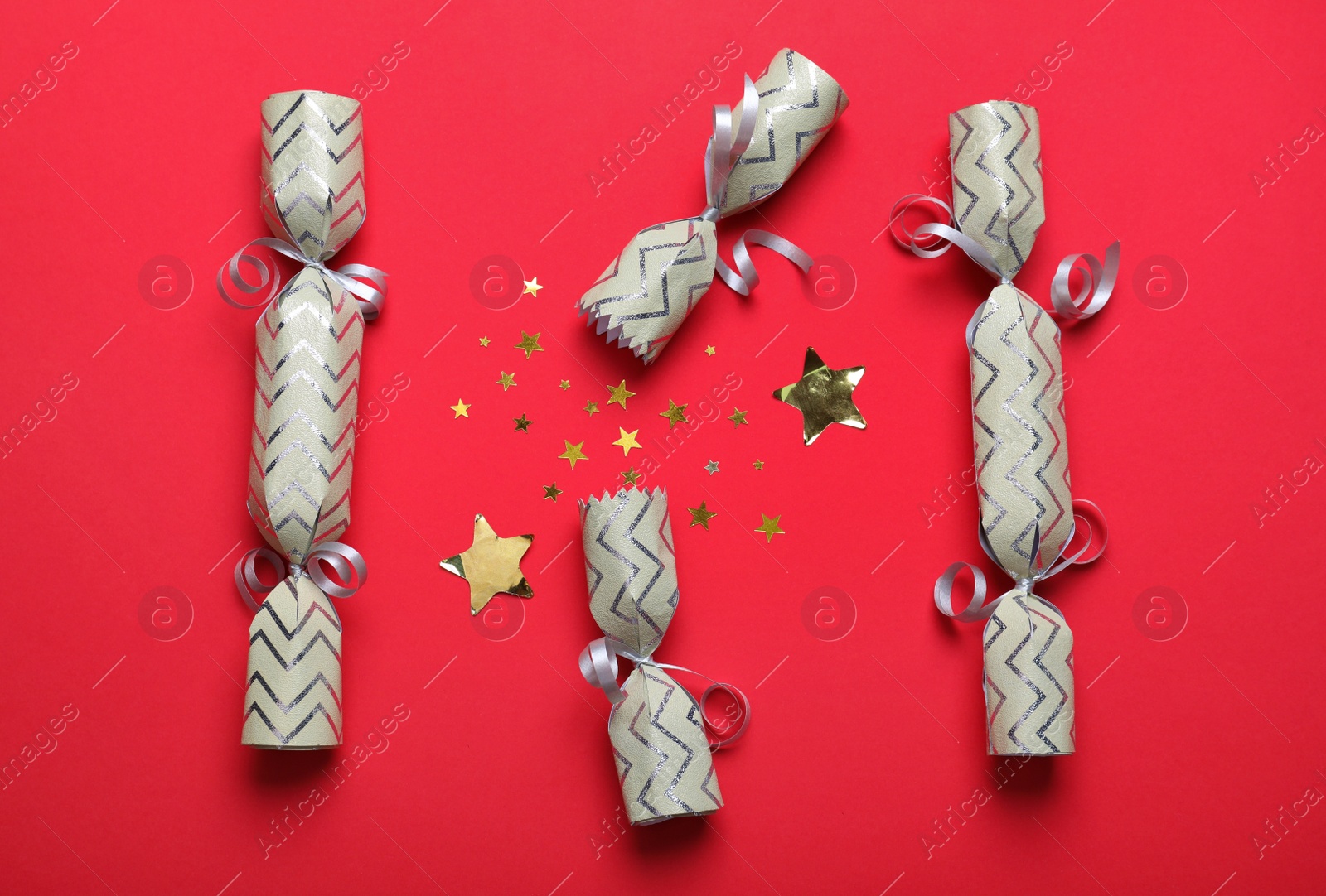 Photo of Open and closed Christmas crackers with shiny confetti on red background, flat lay
