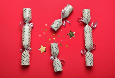 Open and closed Christmas crackers with shiny confetti on red background, flat lay