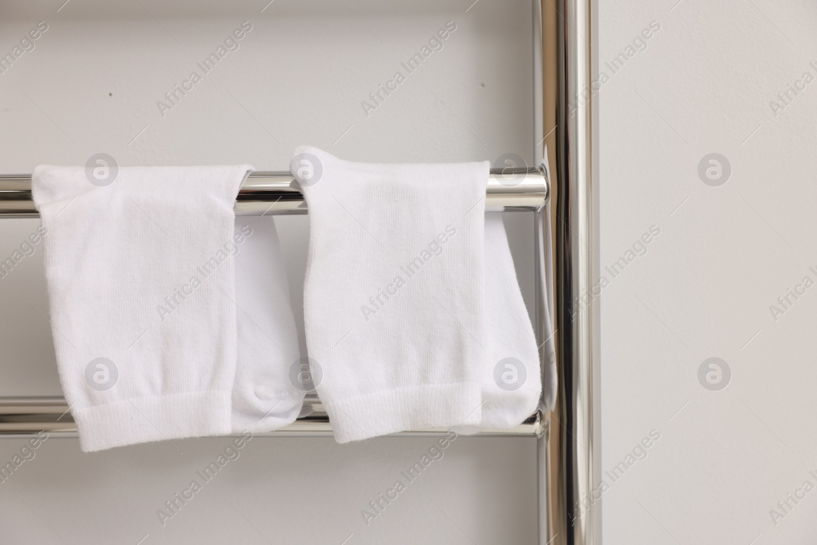 Photo of Heated towel rail with socks on white wall, closeup