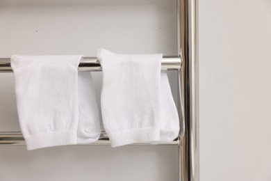Photo of Heated towel rail with socks on white wall, closeup