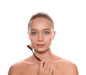 Young woman applying foundation on her face against white background