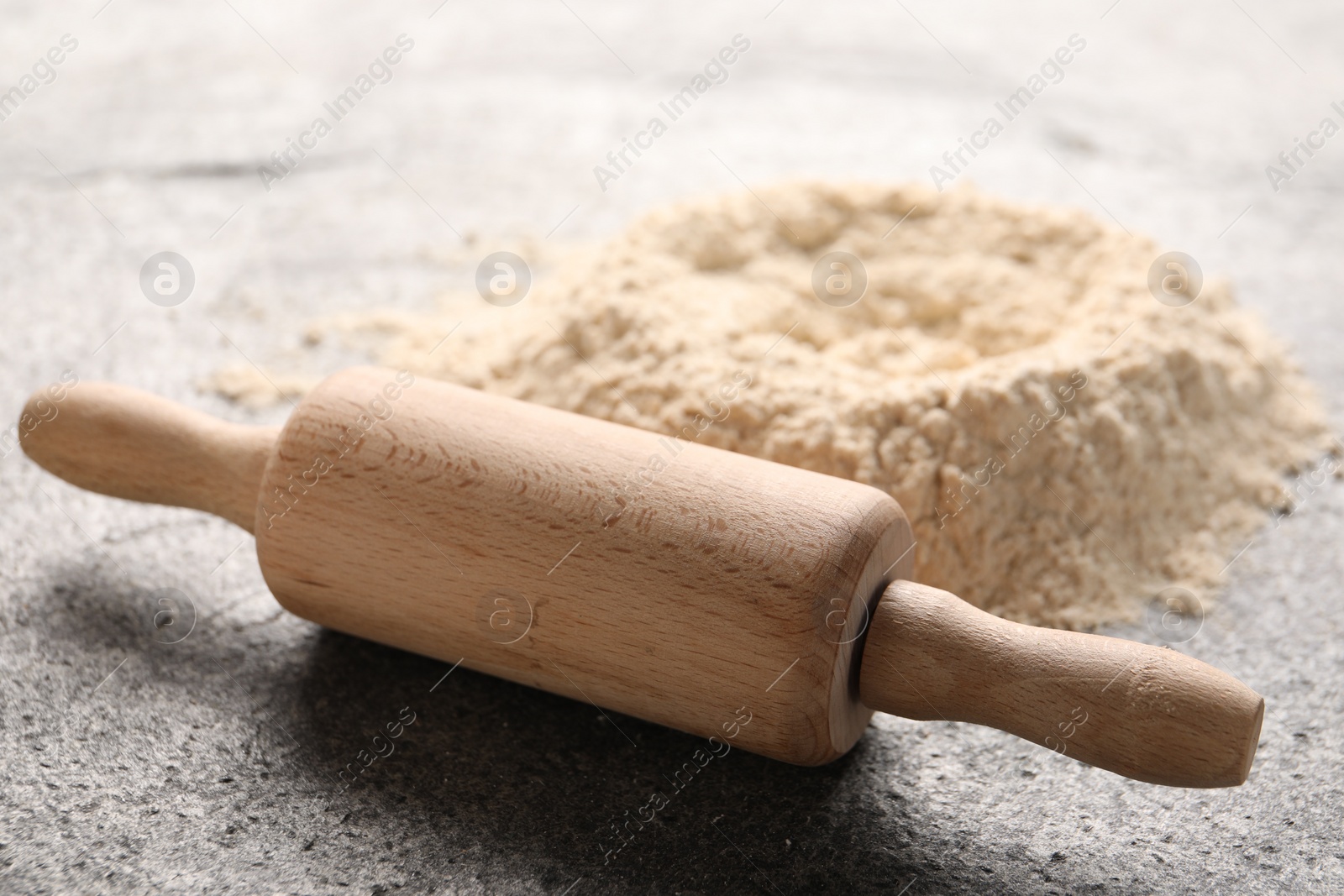 Photo of Rolling pin and scattered flour on grey textured table, closeup