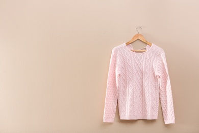 Photo of Hanger with stylish sweater on beige wall. Space for text