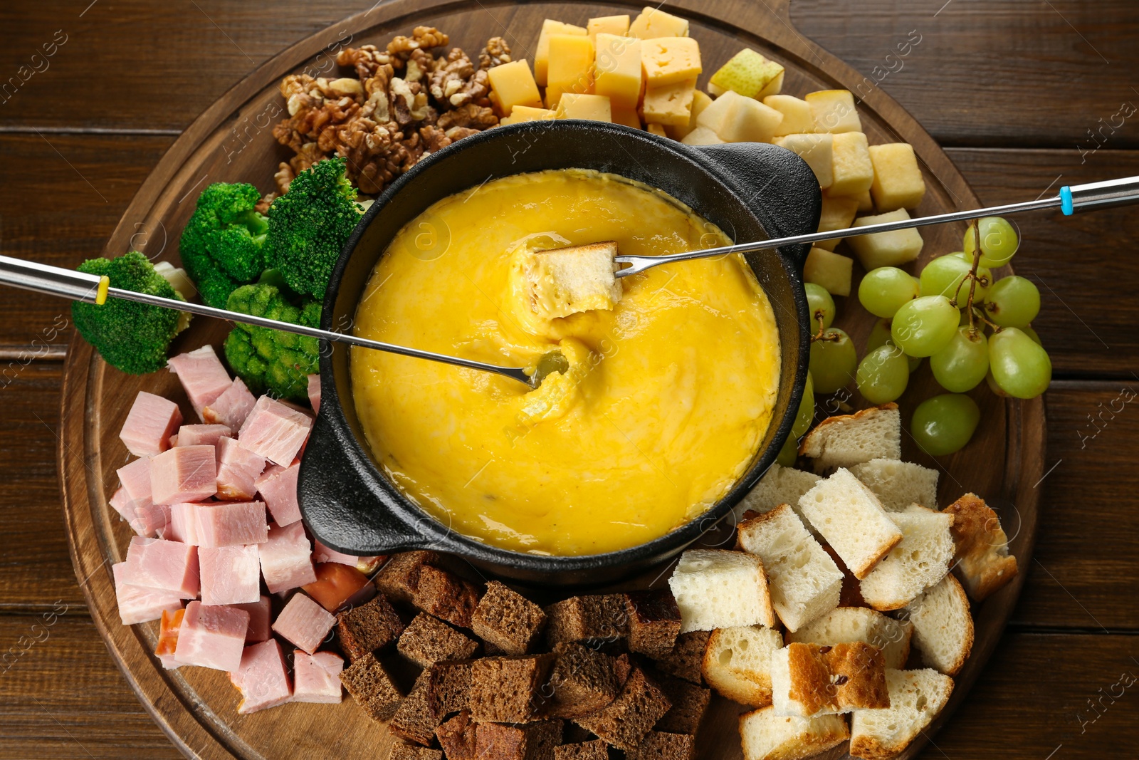 Photo of Fondue pot with melted cheese and different products on wooden table, top view