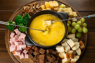 Fondue pot with melted cheese and different products on wooden table, top view