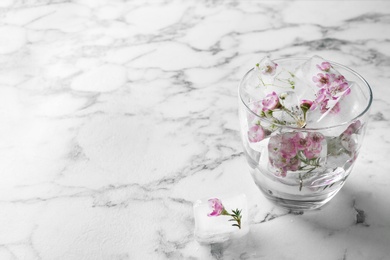 Photo of Glass of water with floral ice cubes on table. Space for text