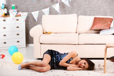 Young woman sleeping on floor in messy room after party