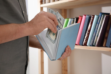 Man hiding money in book indoors, closeup. Financial savings