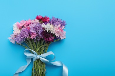 Photo of Bouquet of beautiful cornflowers on light blue background, top view. Space for text