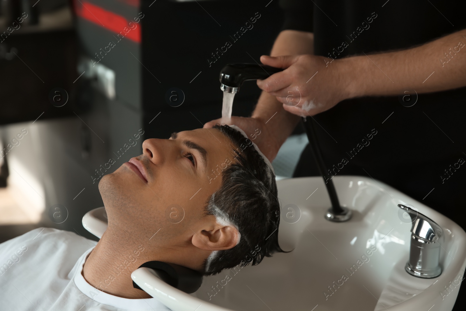 Photo of Professional barber washing client's hair at sink in salon, closeup