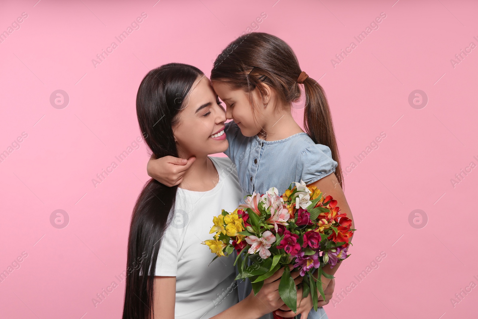 Photo of Happy woman with her daughter and bouquet of flowers on pink background. Mother's day celebration