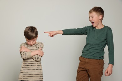 Boy laughing and pointing at upset kid on light grey background. Children's bullying