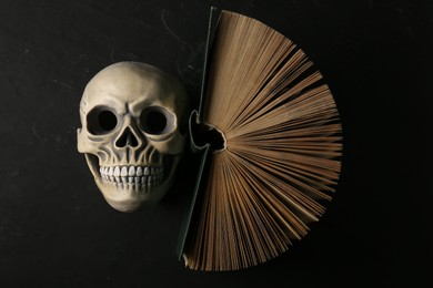 Photo of Human skull and old book on black table, top view