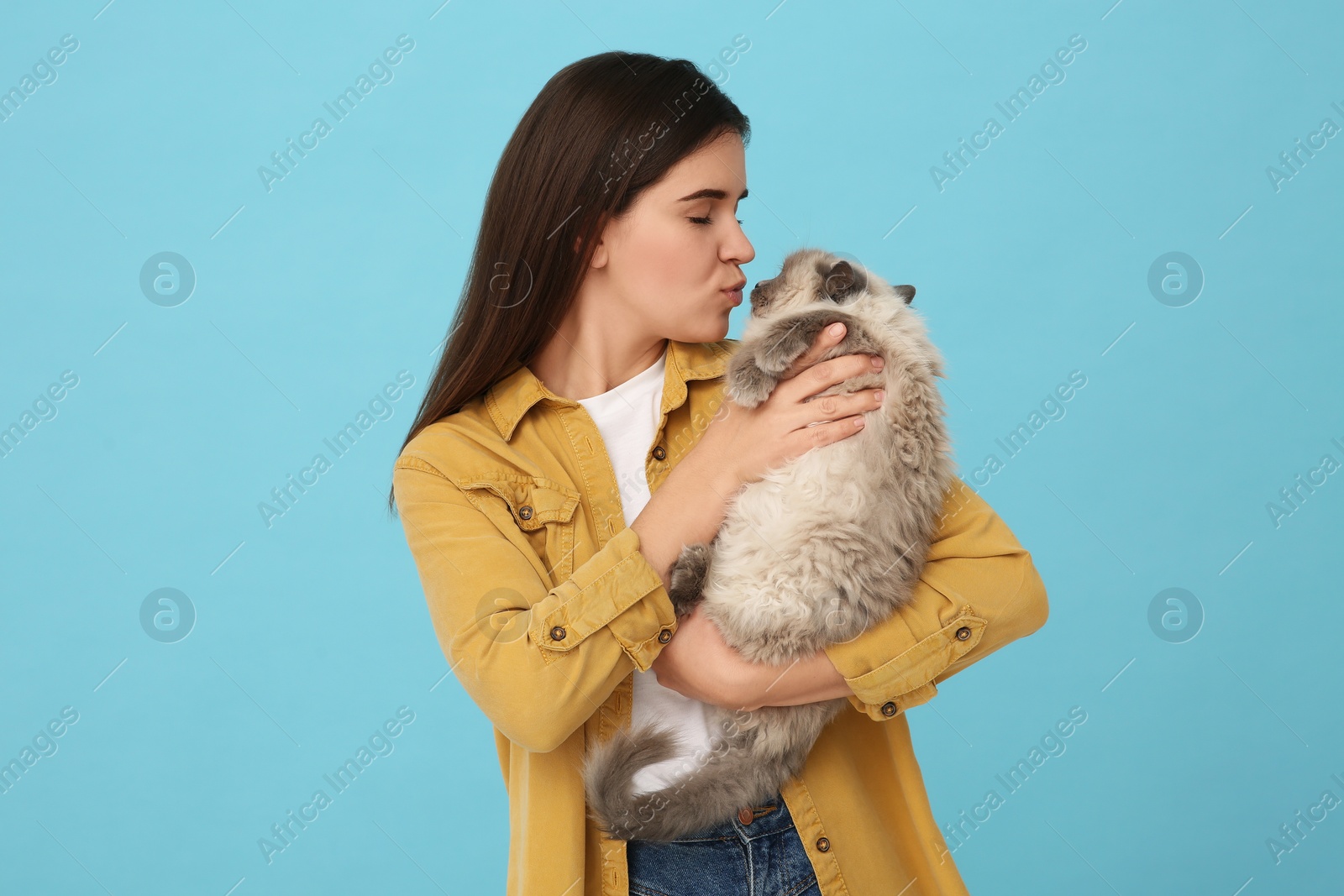 Photo of Woman kissing her cute cat on light blue background