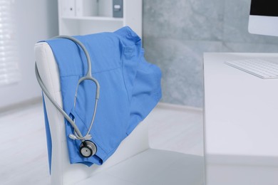 Photo of Blue medical uniform and stethoscope hanging on chair in clinic