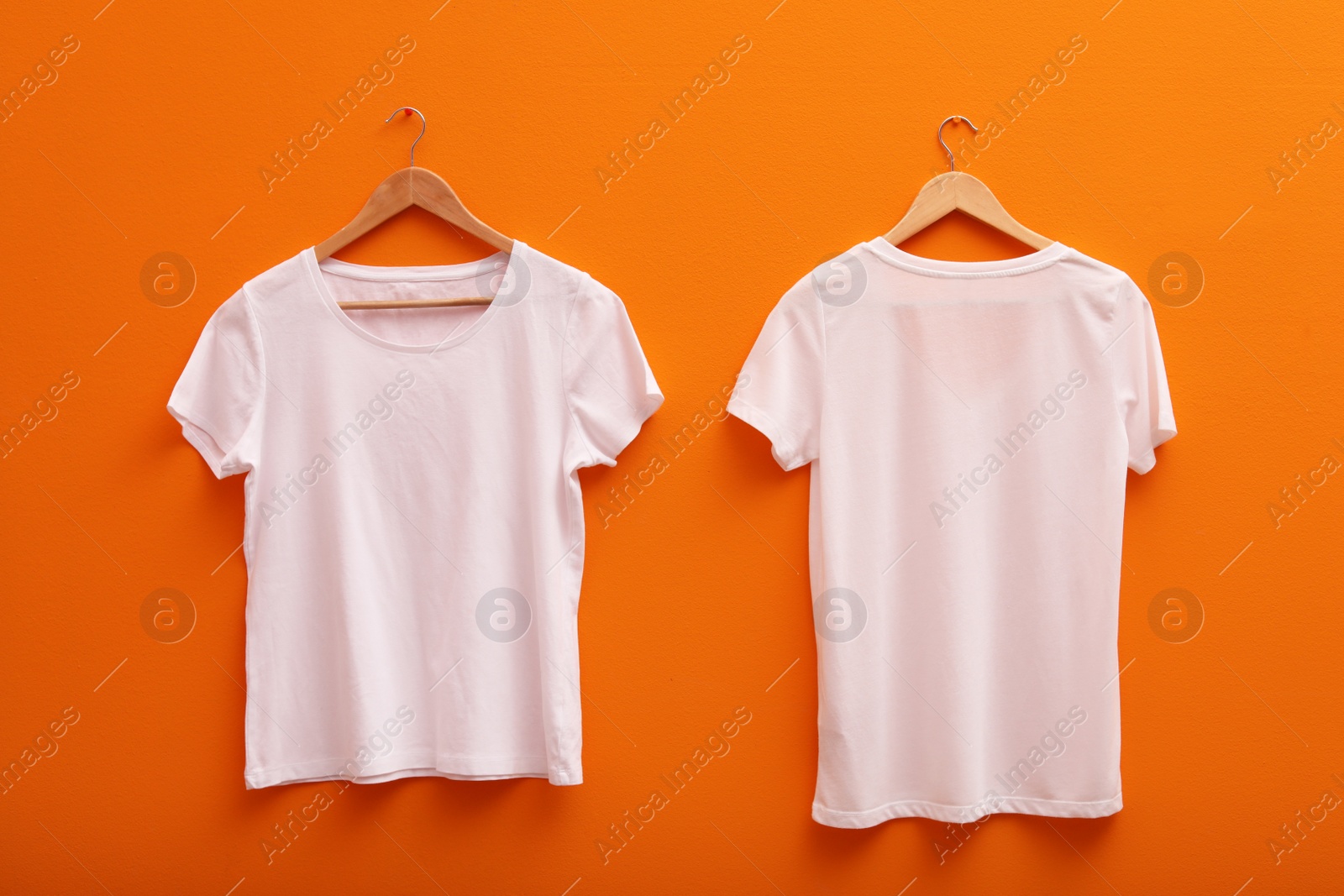 Photo of Hangers with blank t-shirts on color background. Mockup for design