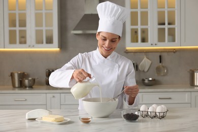 Photo of Professional chef adding milk into dough at white marble table in kitchen