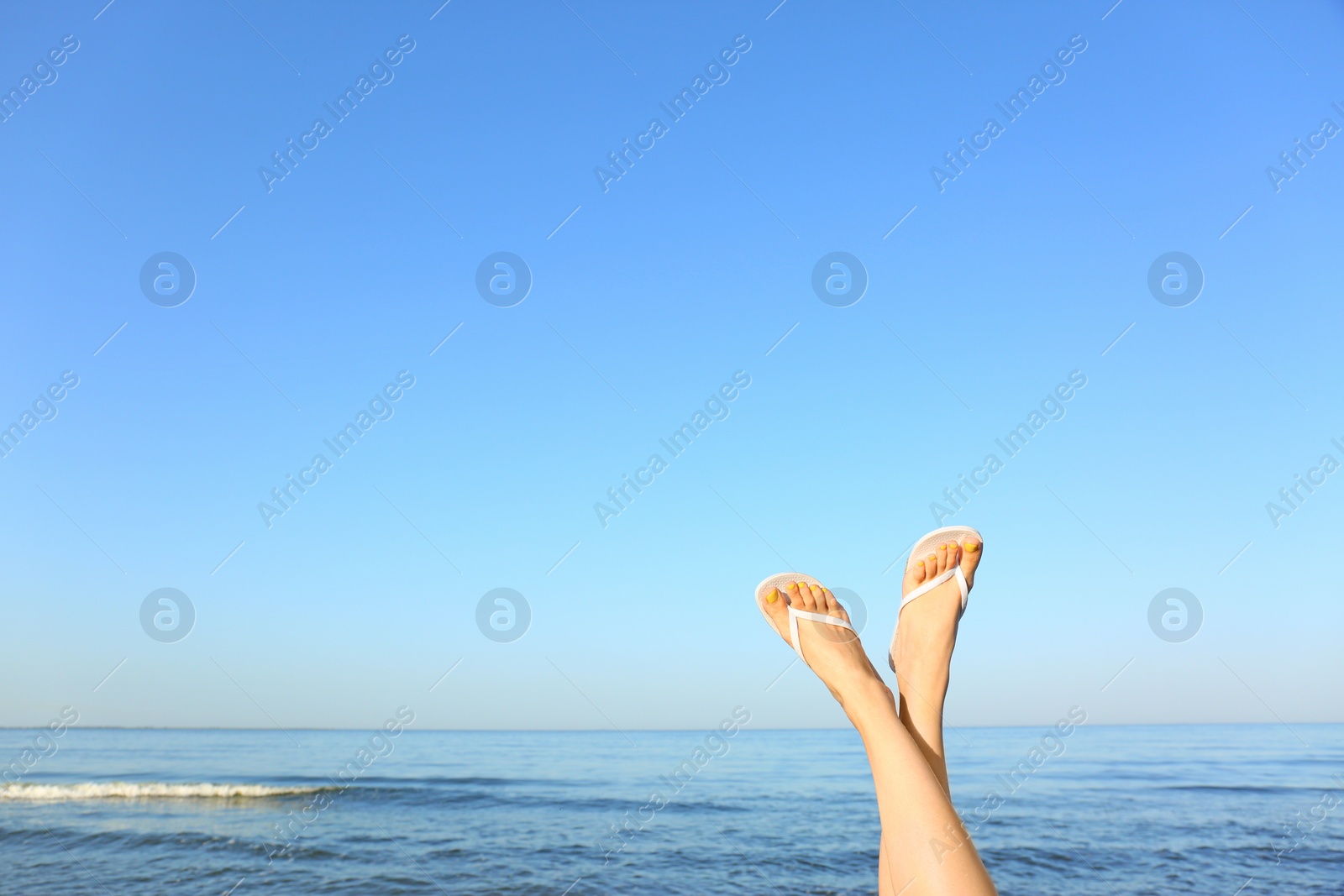 Photo of Closeup of woman wearing flip flops near sea, space for text. Beach accessories