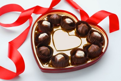 Heart shaped box with delicious chocolate candies and ribbon on light blue background, closeup